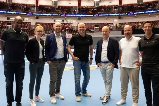 Die Verantwortlichen von Adesso und DHB gemeinsam auf dem Handballfeld. 