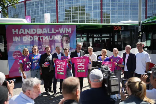 Gruppe posiert vor Westfalenhalle mit Bus im Handball-WM 25 Branding